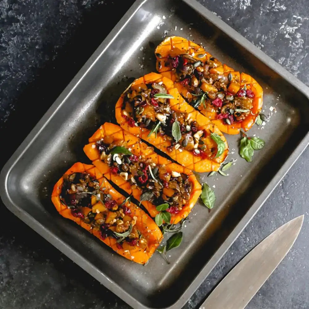 Roasted sweet potatoes topped with herbs and spices on a dark baking tray.