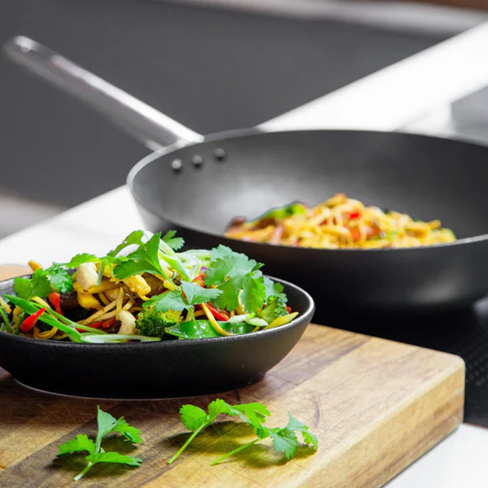 Two black frying pans with stir-fry on a wooden cutting board