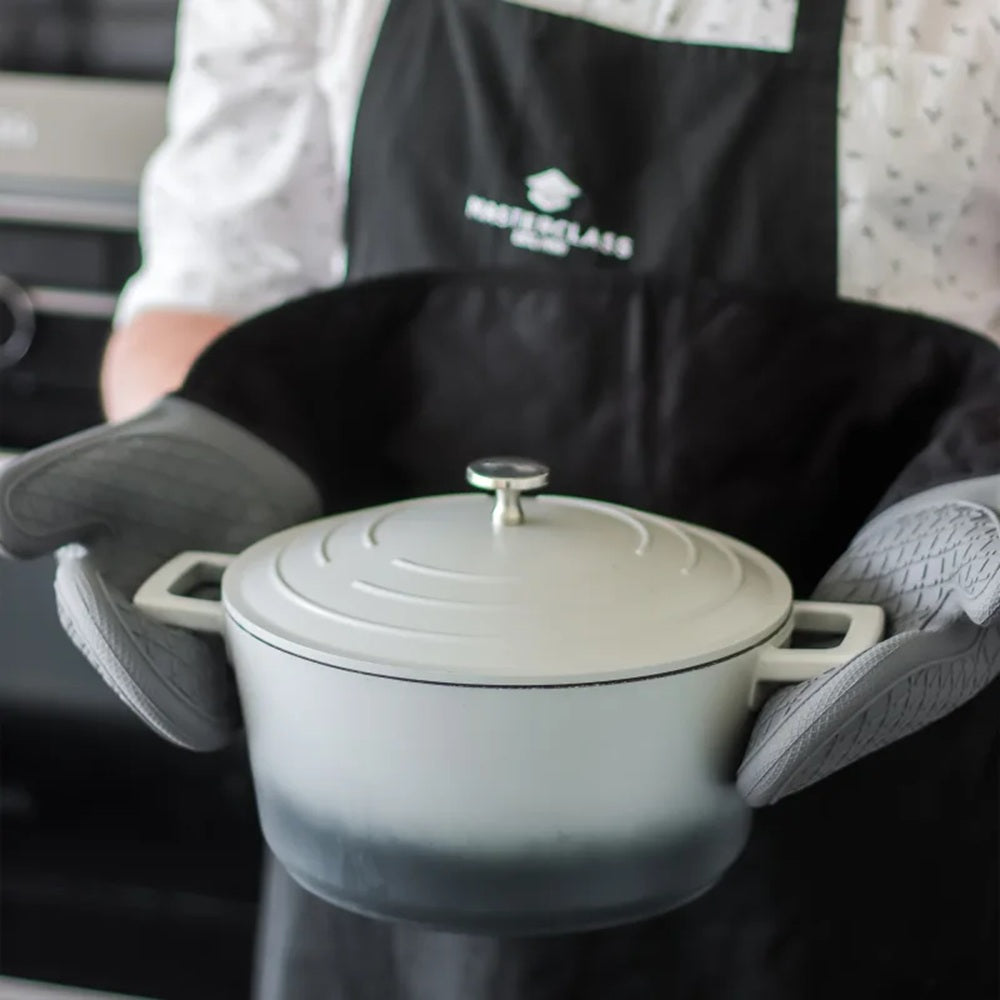 Person holding a green pot with a lid, wearing an apron and oven mitts.