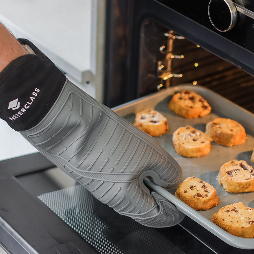 Person wearing a MasterClass oven mitt removing a tray of cookies from an oven.