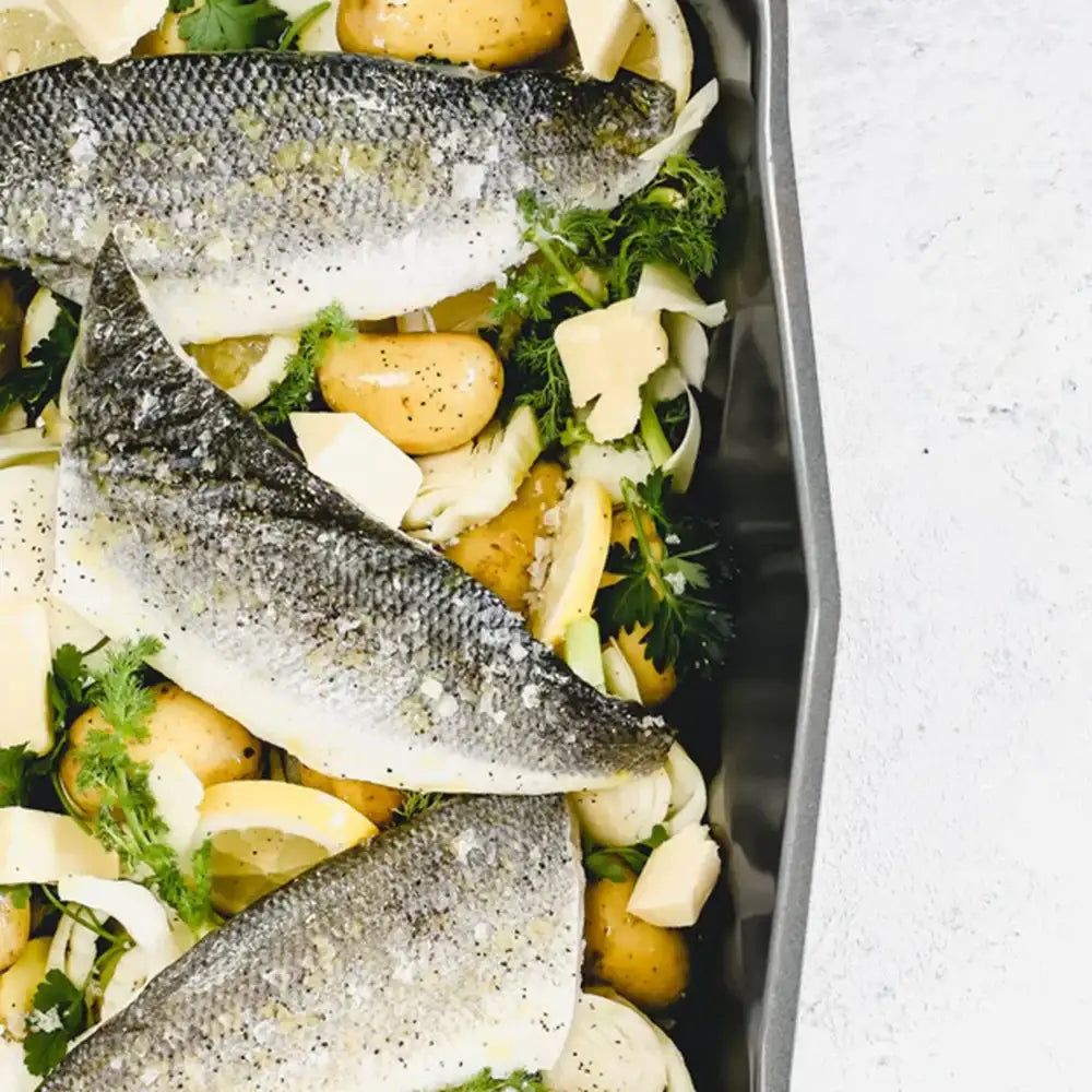 Raw fish fillets on a bed of vegetables in a baking dish.