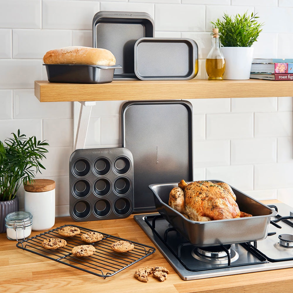 Kitchen scene with baking trays, a roasted chicken, and plants on a wooden shelf.