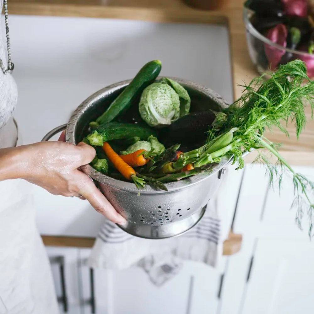Colander with vegetables held by a hand on a kitchen counter