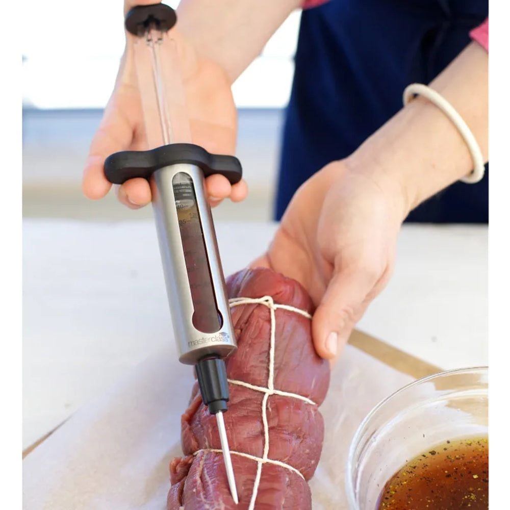 Person using a meat Injector to inject marinade into a piece of meat on a white surface.