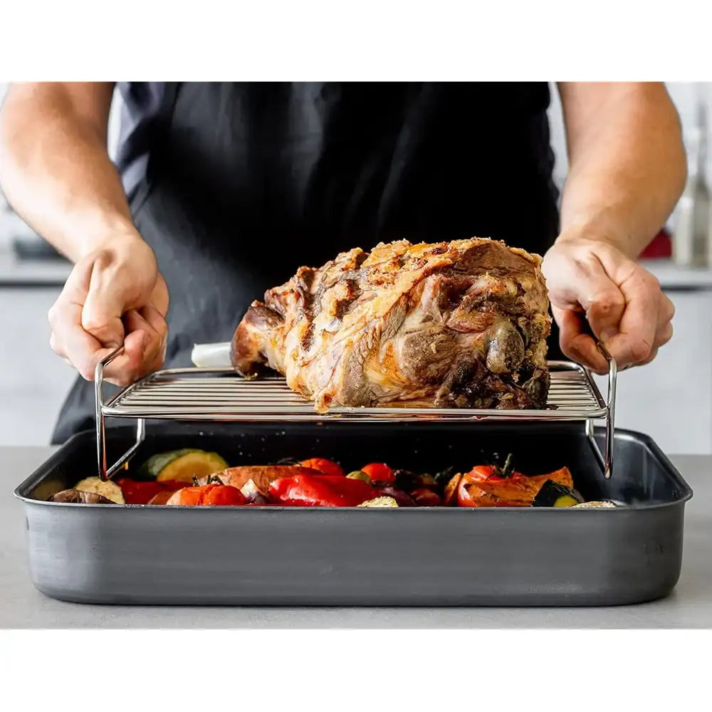 Person placing a roasted lamb leg onto a roasting pan with vegetables.