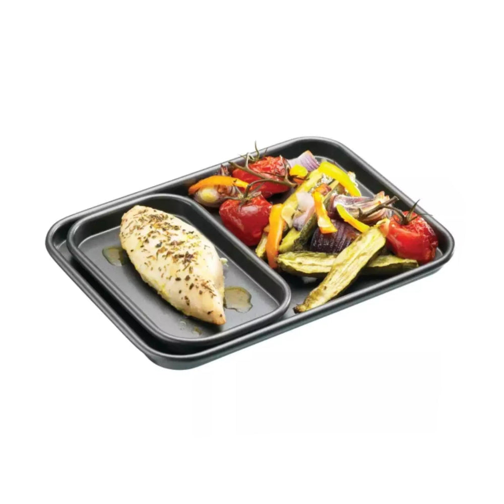 MasterClass Non-Stick Baking Tray 39x27x2cm with a smaller tray on it and fish and chips on a white background
