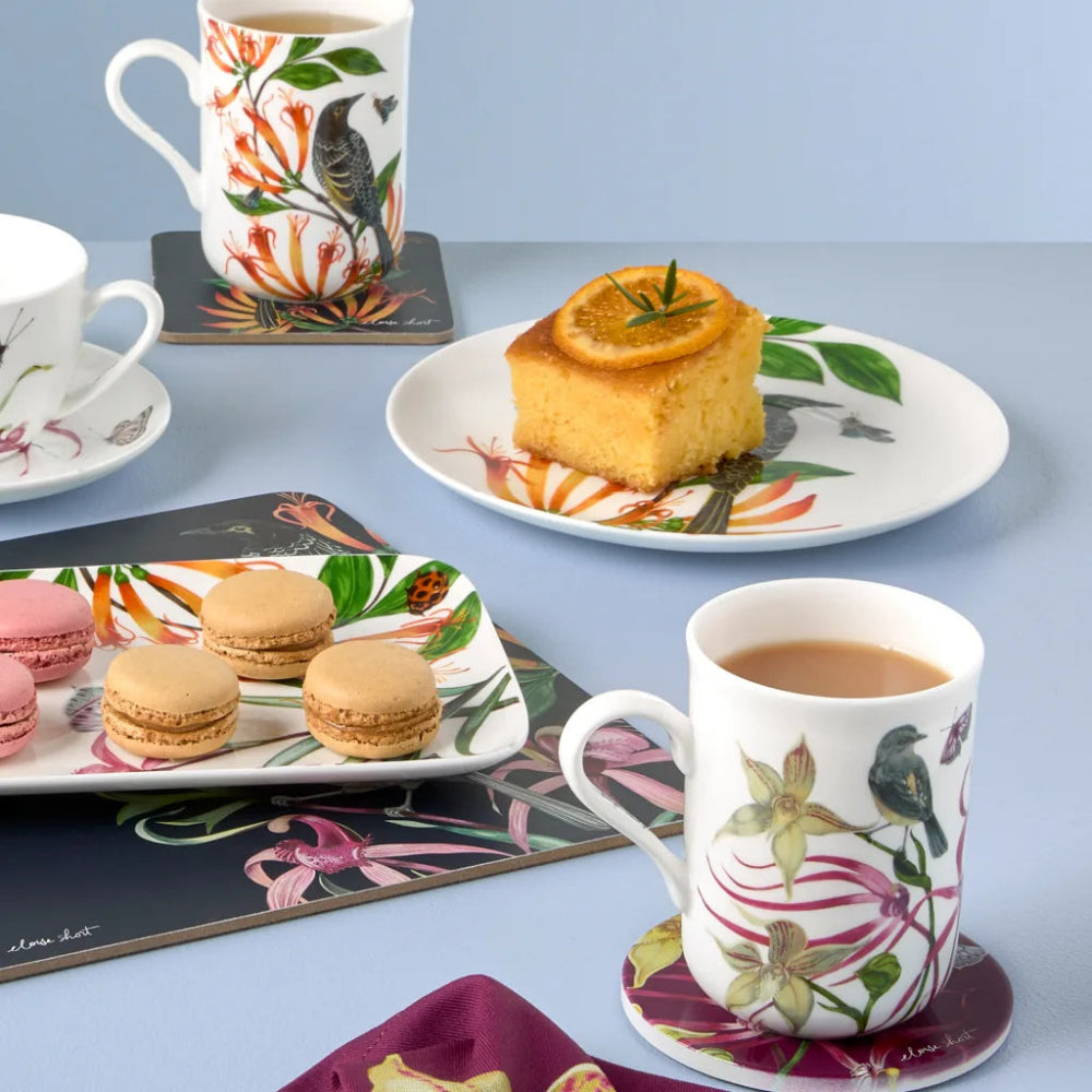 Tea set with floral mugs, cookies, and a cake on a light blue background
