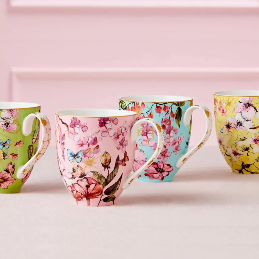 Four colorful mugs with floral and butterfly designs on a pink background