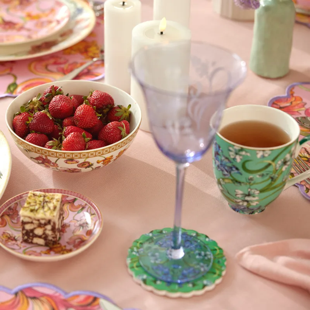 Table setting with strawberries, a glass of tea, and a piece of cake on a colorful tablecloth.