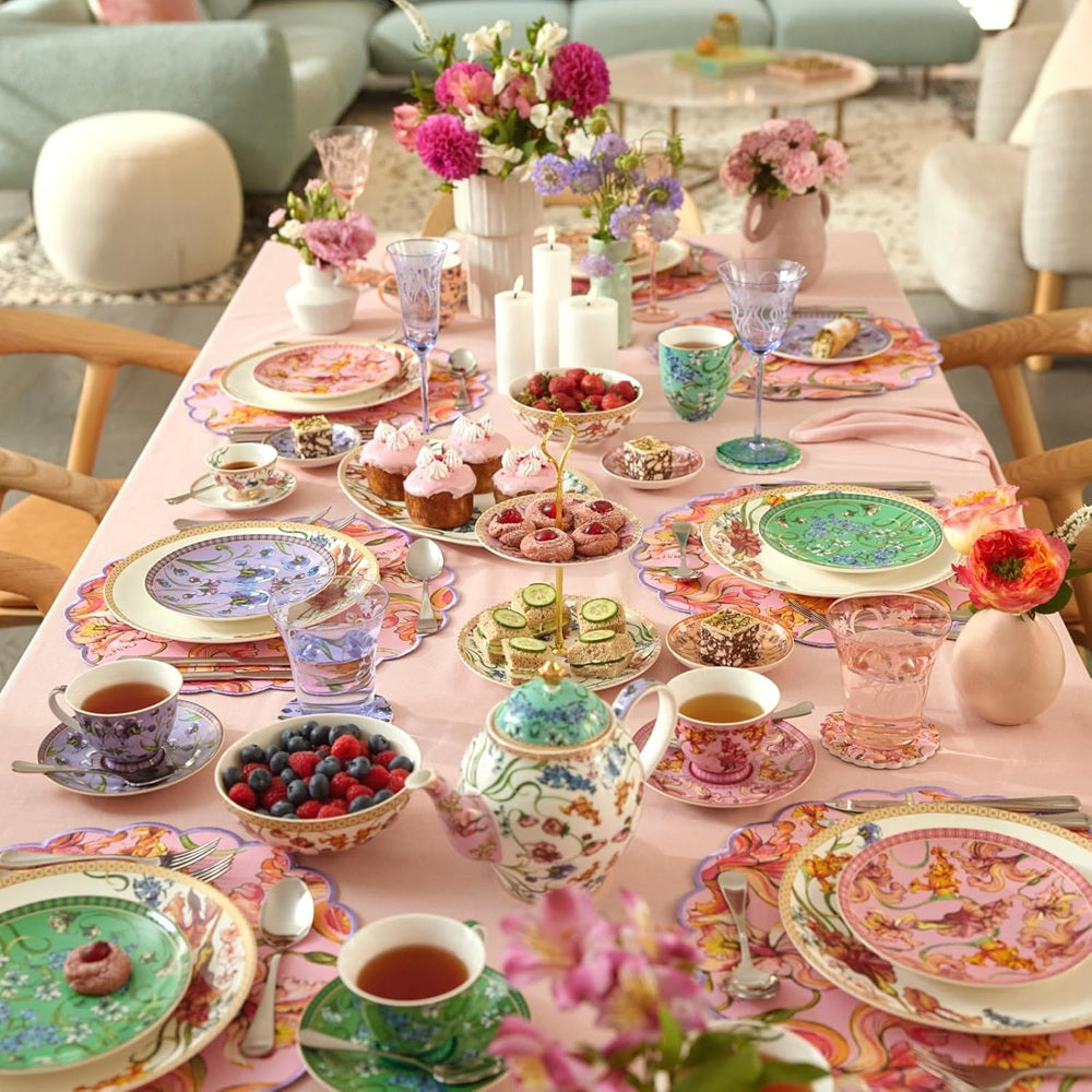 Decorative table setting with floral arrangements, teacups, and pastries in a cozy room.