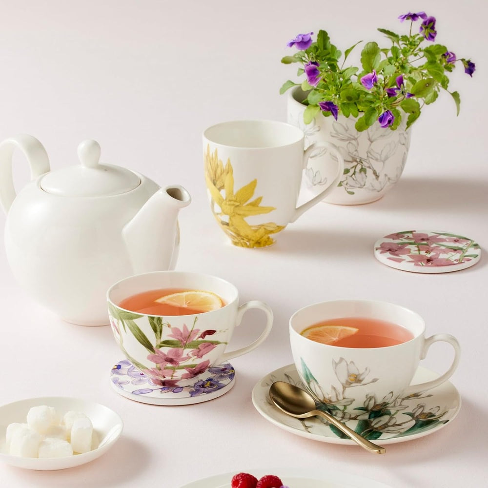 Tea set with floral cups, teapot, and a plant on a light background