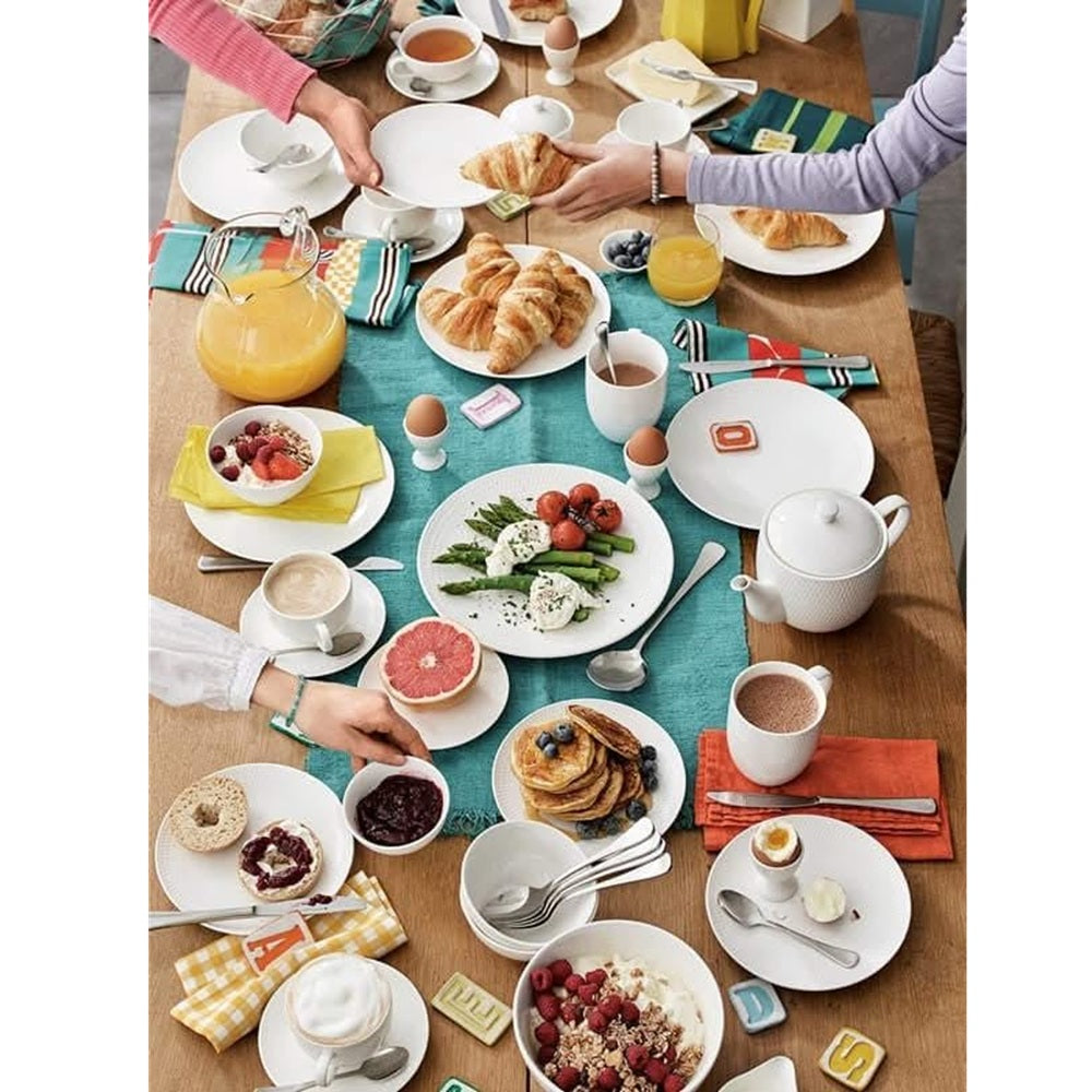 Table set for breakfast with various dishes and people around it.