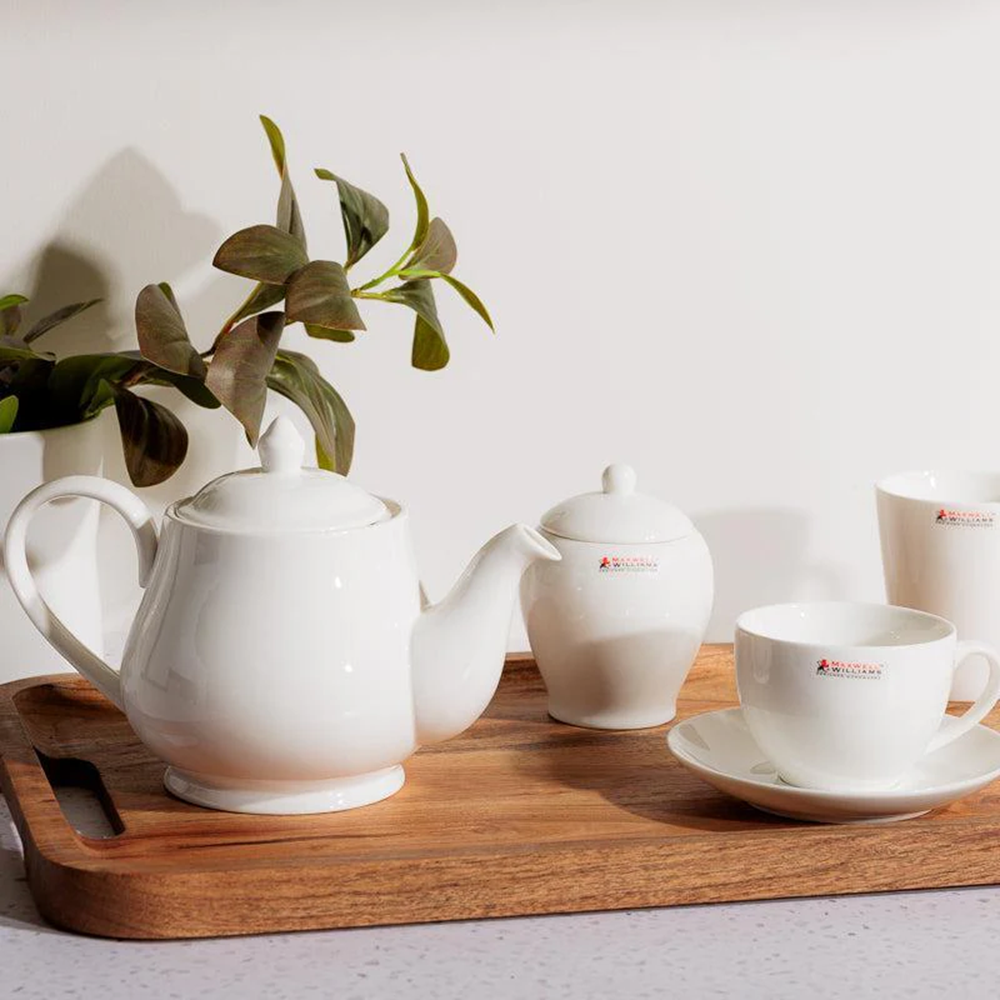 White ceramic tea set on a wooden tray with a plant in the background