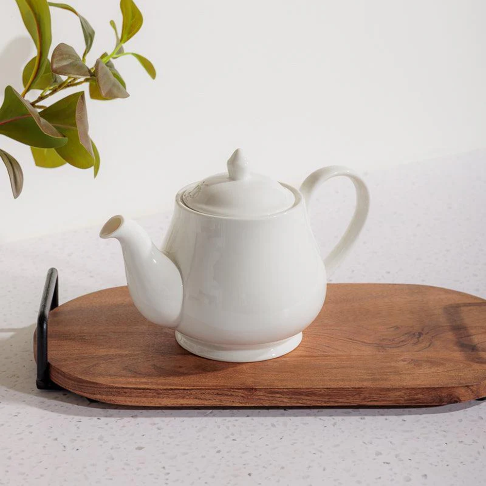 White teapot on a wooden tray with a plant in the background