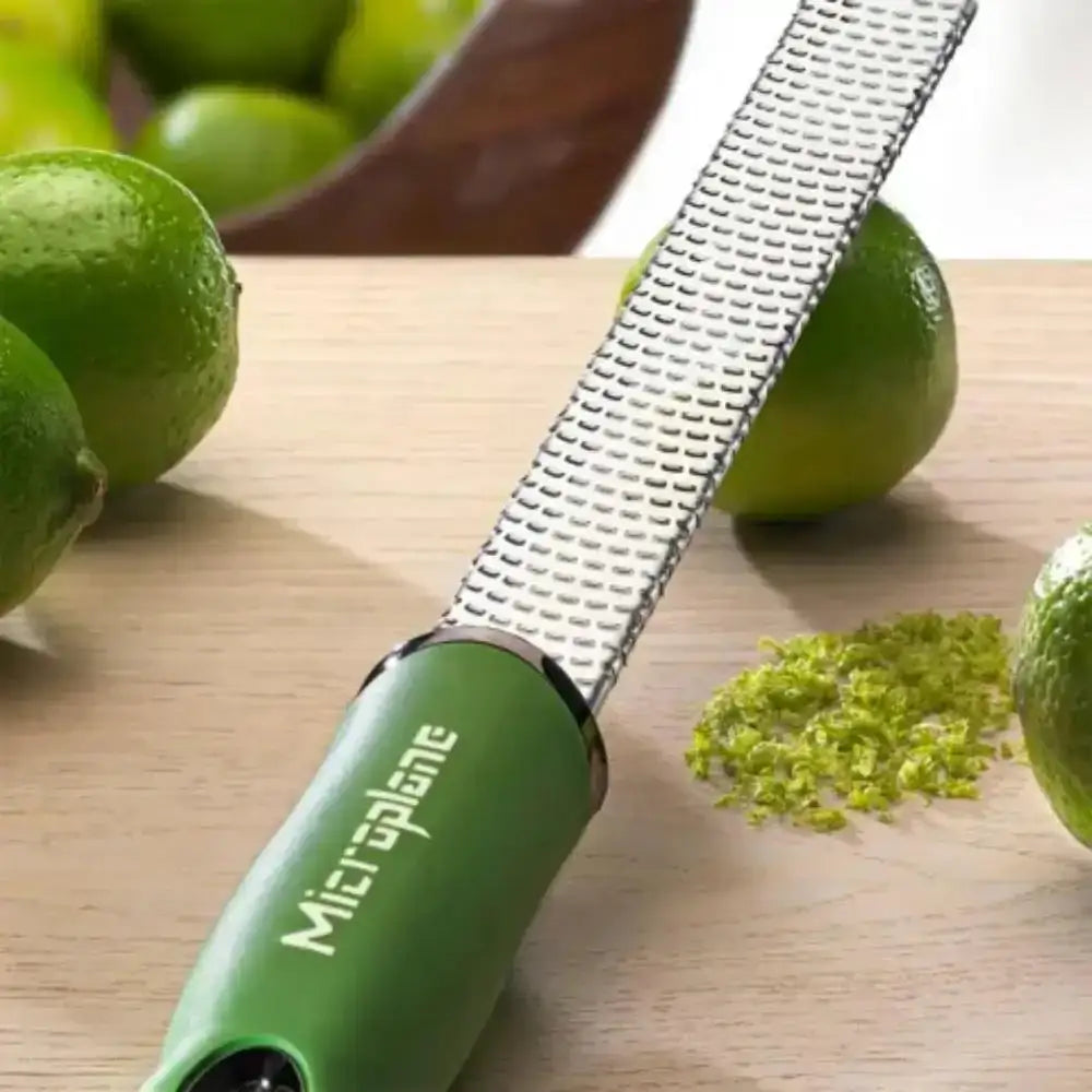 Green microplane grater with lime zest on a wooden surface