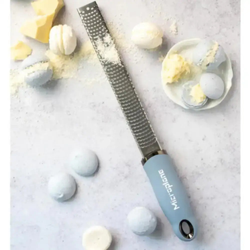 Blue microplane grater on a light gray surface with powdered sugar and confectionery items.