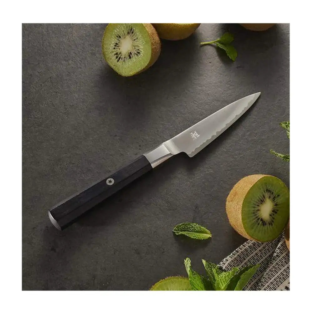 Knife with a black handle on a dark surface surrounded by kiwis