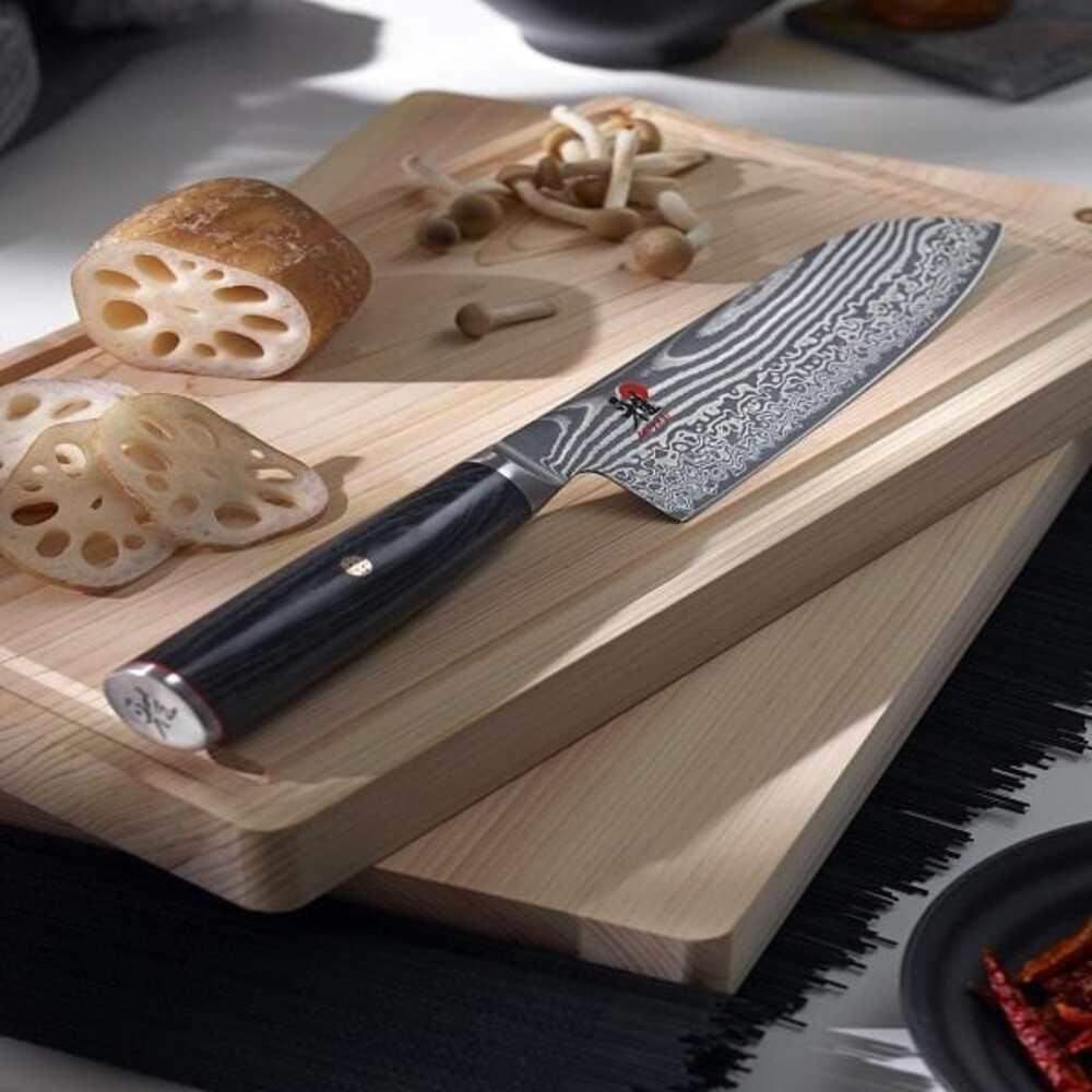 Chef's knife on a wooden cutting board with sliced lotus root and mushrooms.