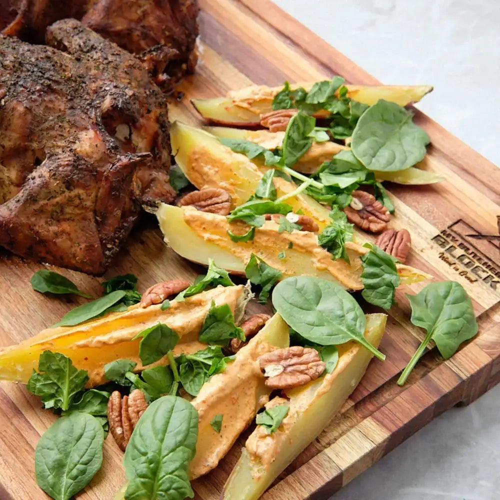 Wooden cutting board with roasted vegetables, greens, and pecans on a marble surface