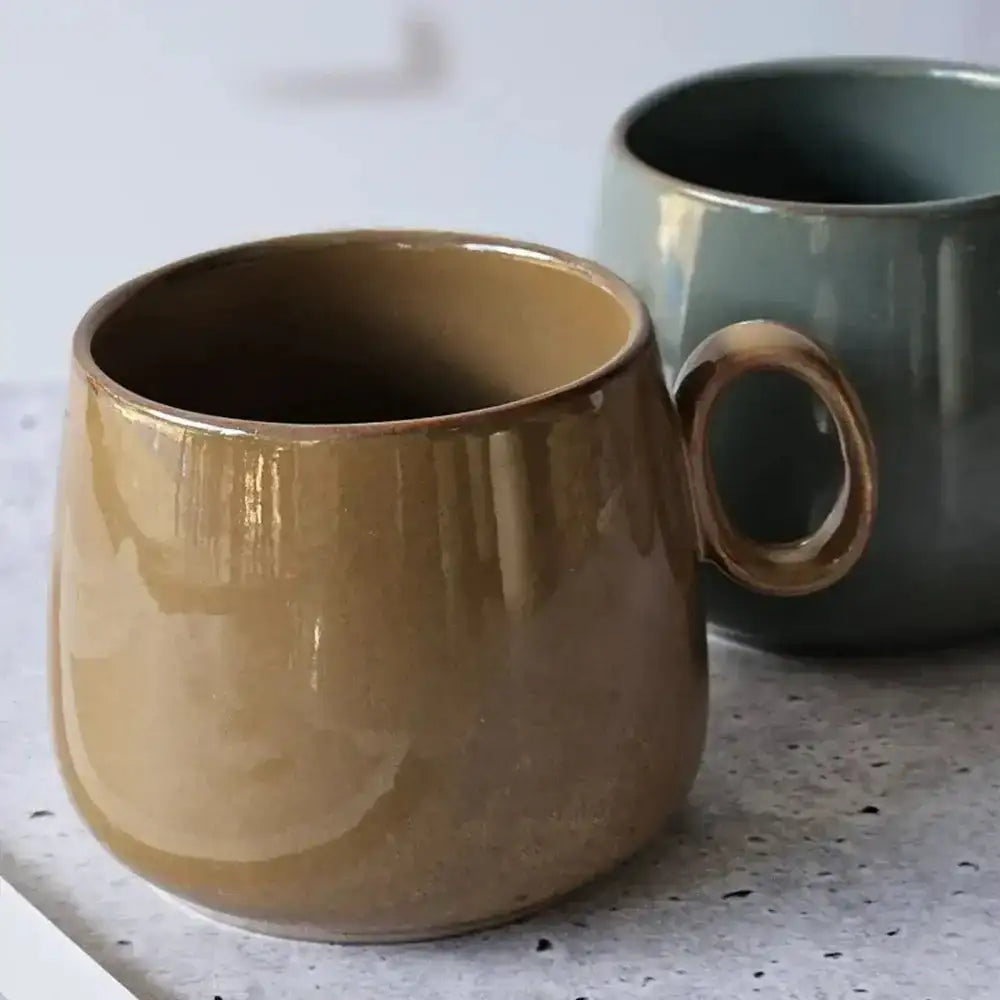 Two ceramic mugs, one brown and one green, on a speckled countertop.