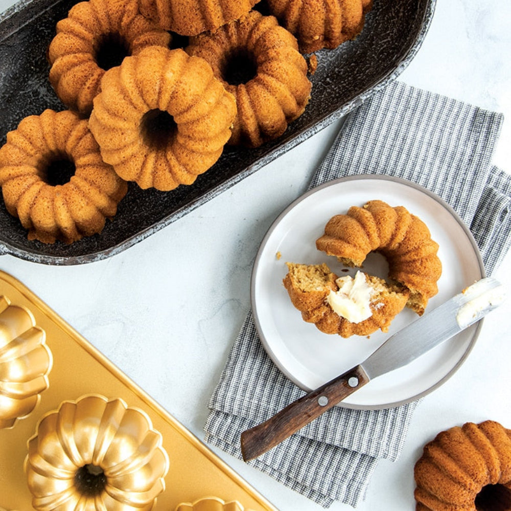 Bundt cakes in a pan with one on a plate, surrounded by a cake pan and knife.