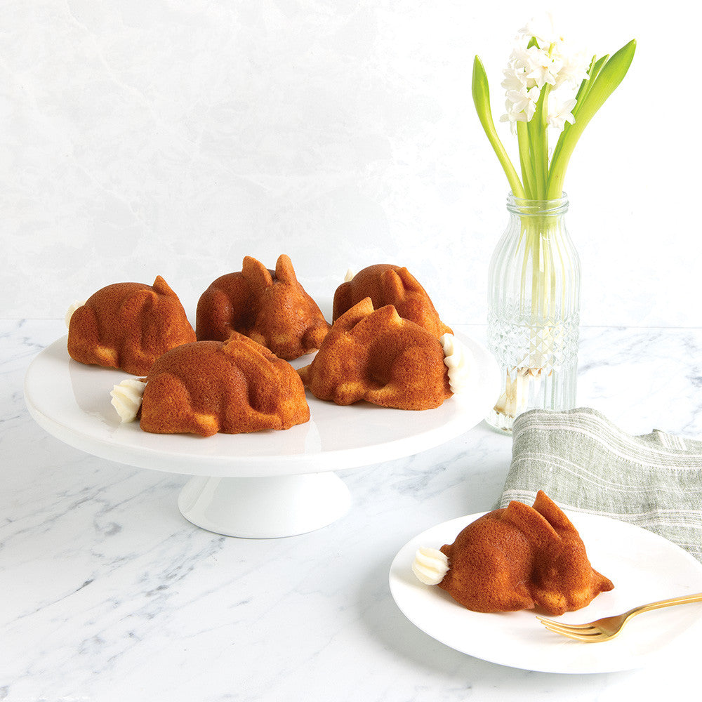 Small bundt cakes shaped like dogs on a white plate with a vase of flowers in the background.