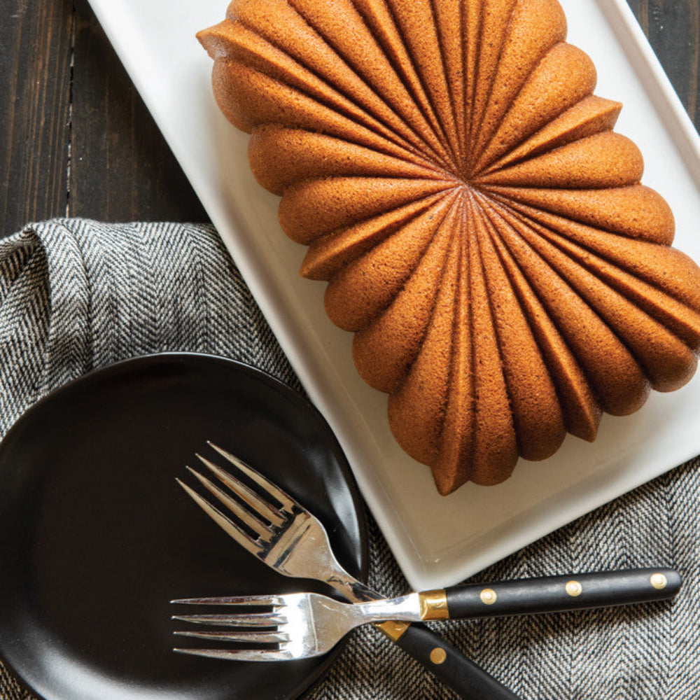 Bundt cake on a white plate with black plates and forks on a checkered tablecloth.