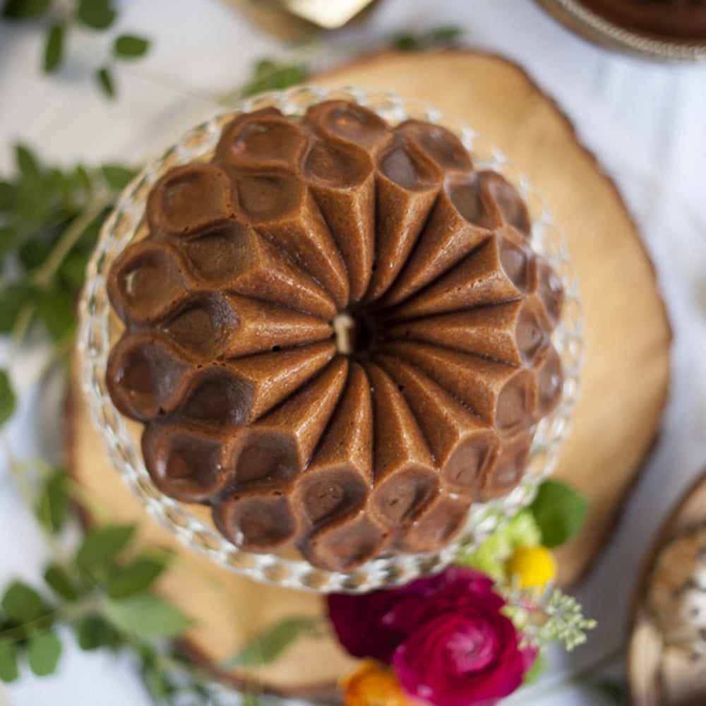 Chocolate cake with a unique spiral design on a wooden stand with flowers in the background