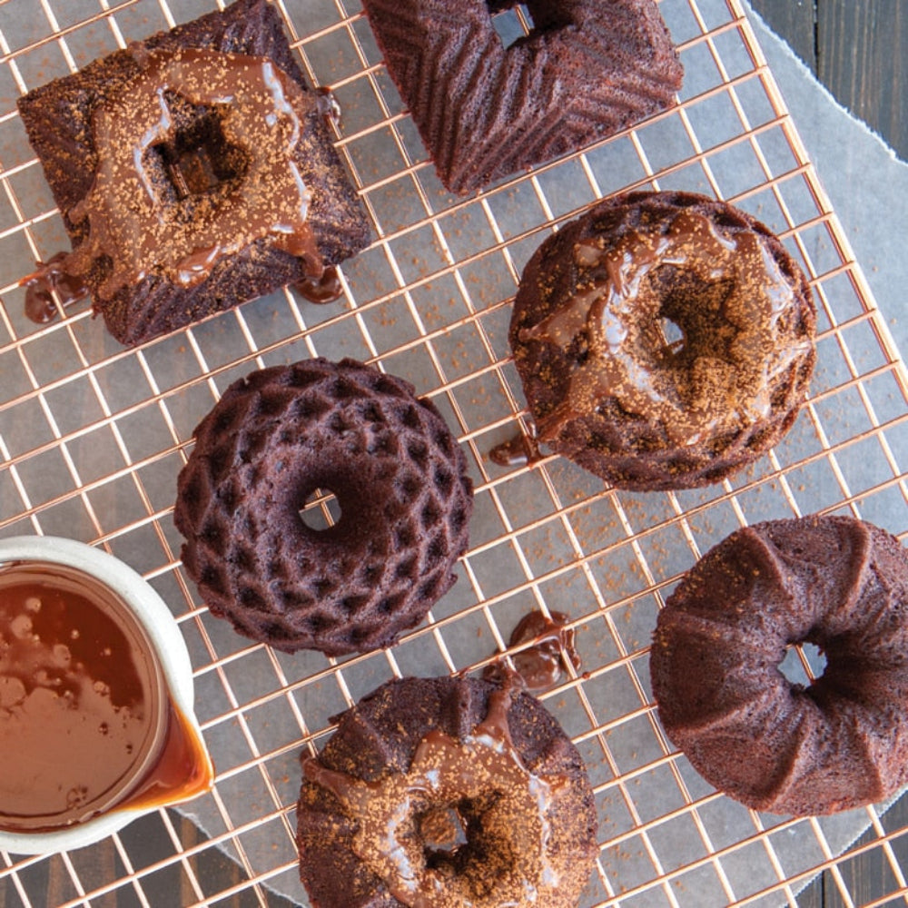 Chocolate mini bundt cakes on a cooling rack with a small bowl of glaze.