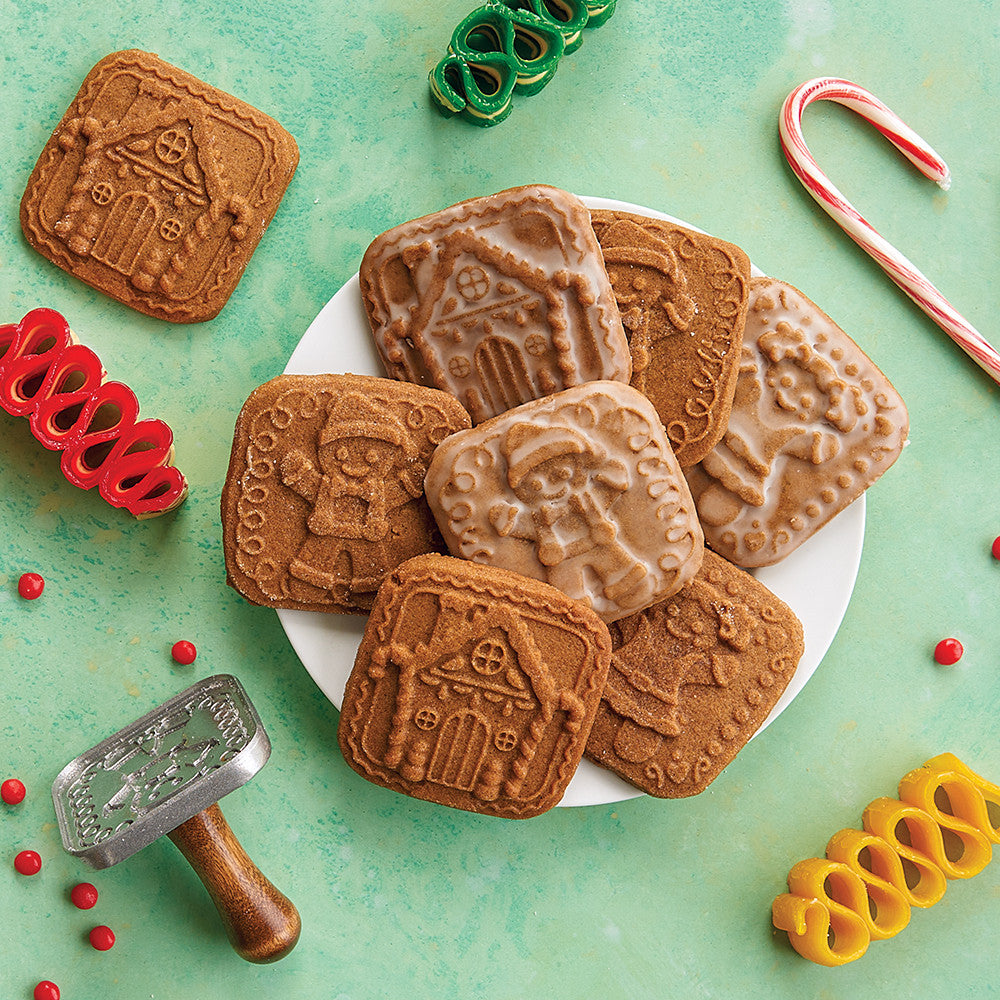 Decorative cookies with house designs on a plate, surrounded by cookie cutters and candy canes on a green background.