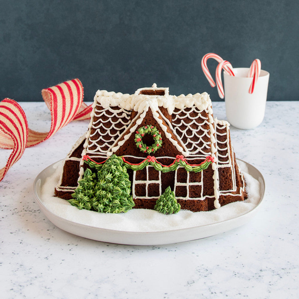Decorated gingerbread house on a white counter with candy cane sweets in the background