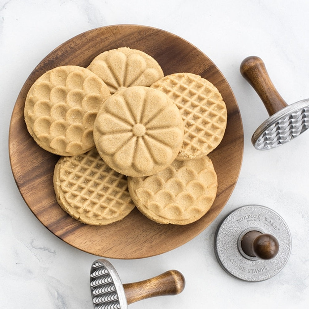 Wooden plate with waffle cookies and cookie cutters on a white background