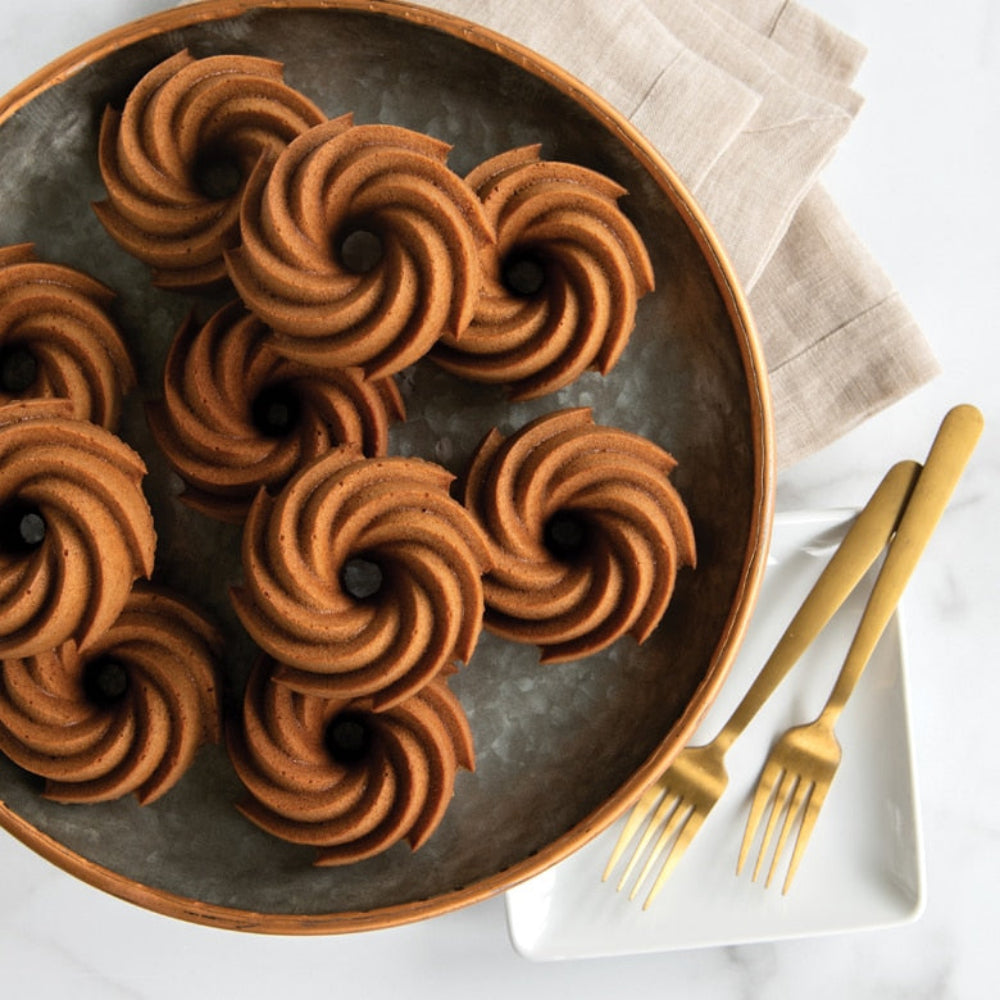 Round metal tray with brown spiral cookies on a white surface with gold forks.