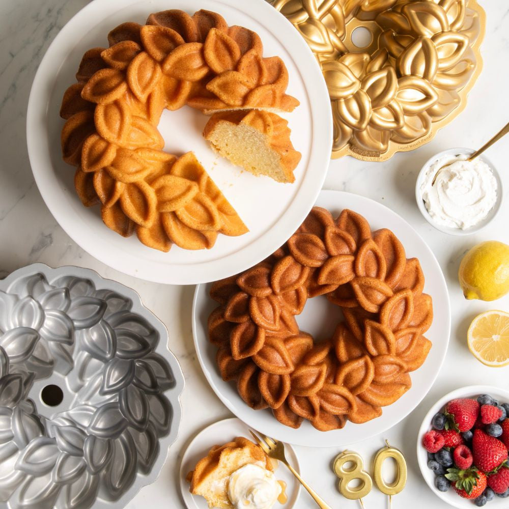 Decorative bundt cakes on white plates with cake pans and fruits on a marble surface