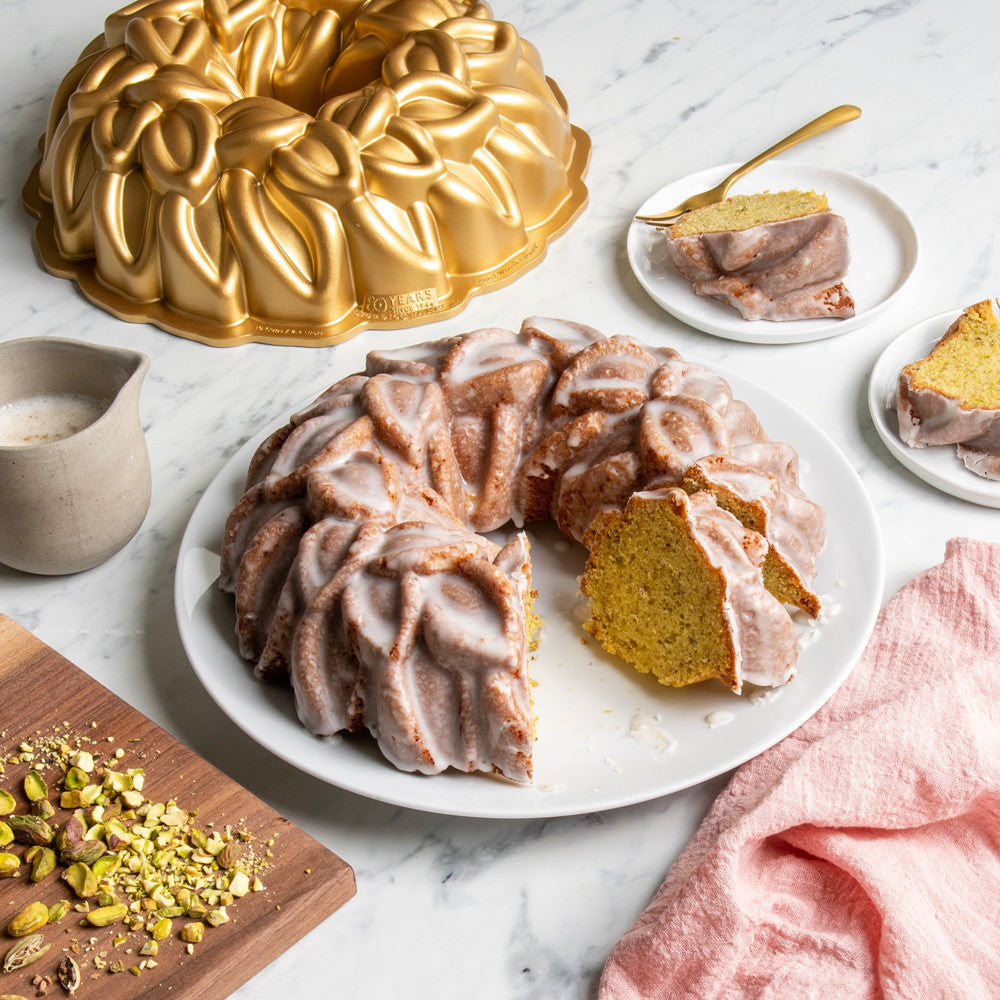Bundt cake with glaze on a white plate, surrounded by baking tools and ingredients on a marble surface.
