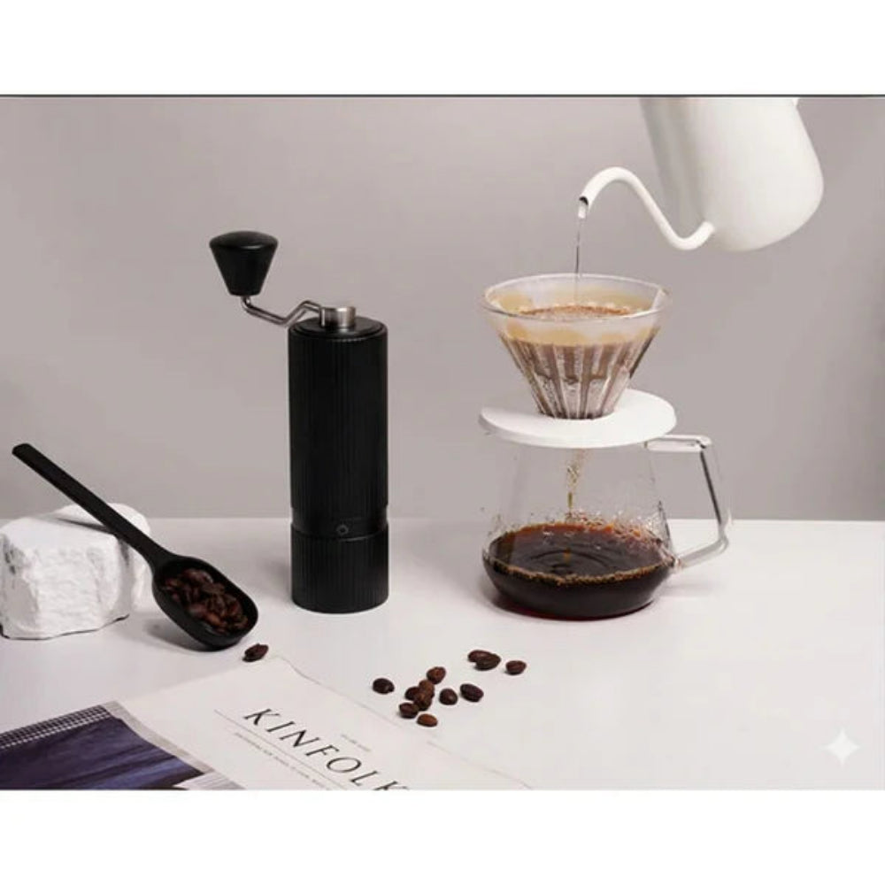 Coffee-making setup with a grinder, coffee beans, and a pour-over coffee setup on a white surface.