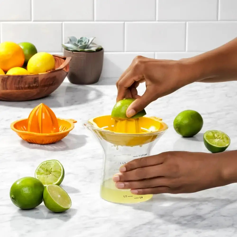 Person using a yellow manual juicer to extract juice from limes on a kitchen counter.