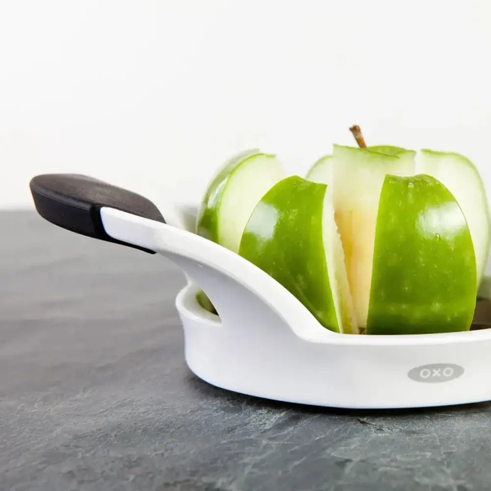 Green apple sliced with a white OXO apple slicer on a gray surface