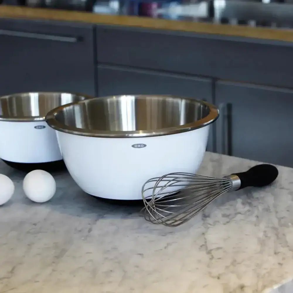 Two stainless steel mixing bowls with a whisk on a kitchen counter.