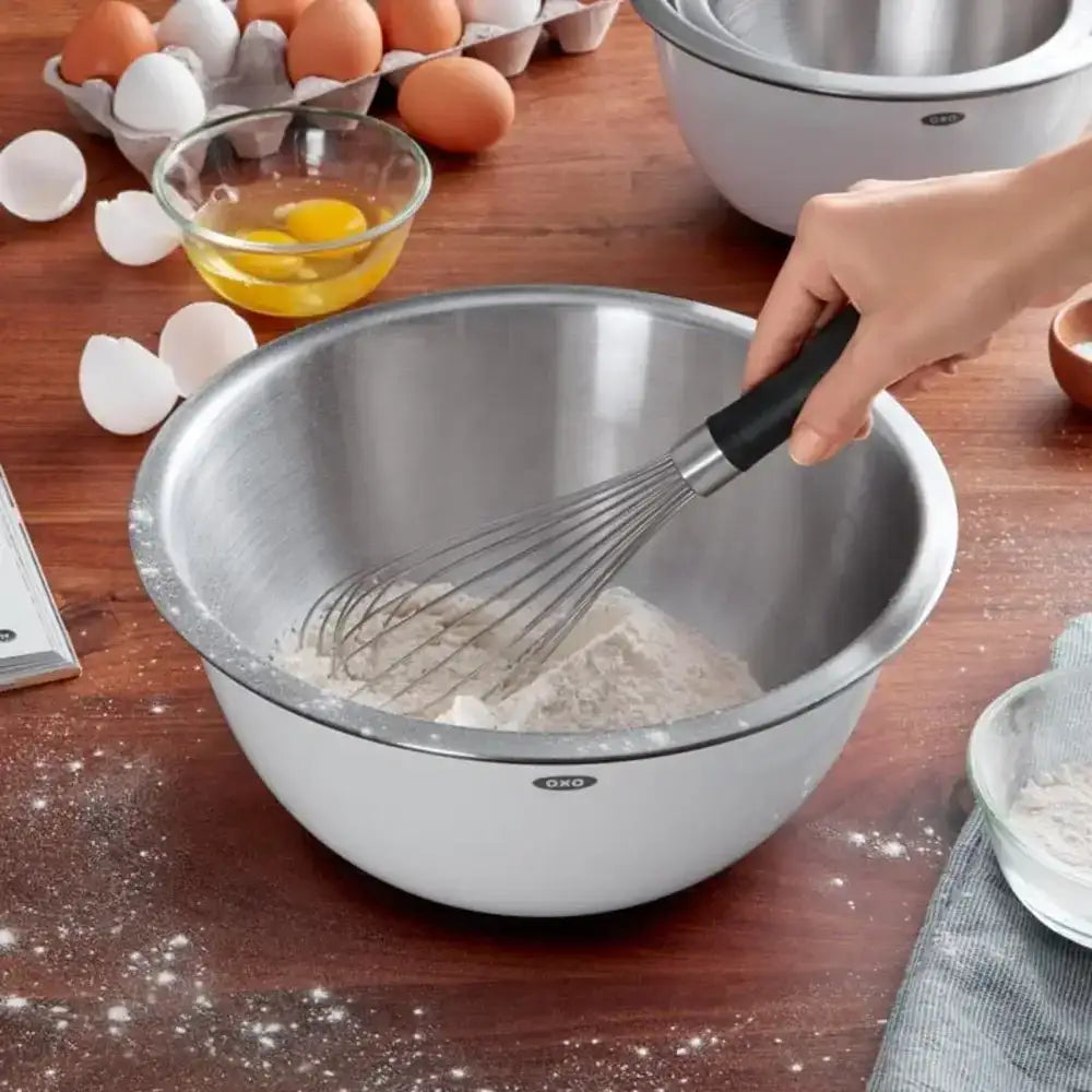 Stainless steel mixing bowl with whisk on a wooden table with ingredients