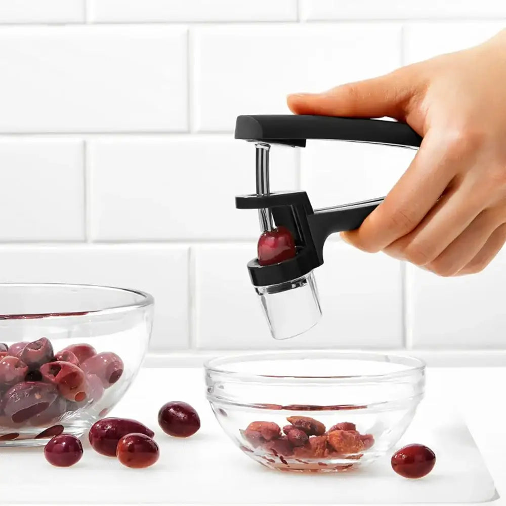 Hand using a cherry pitter to remove pits from cherries on a white surface.