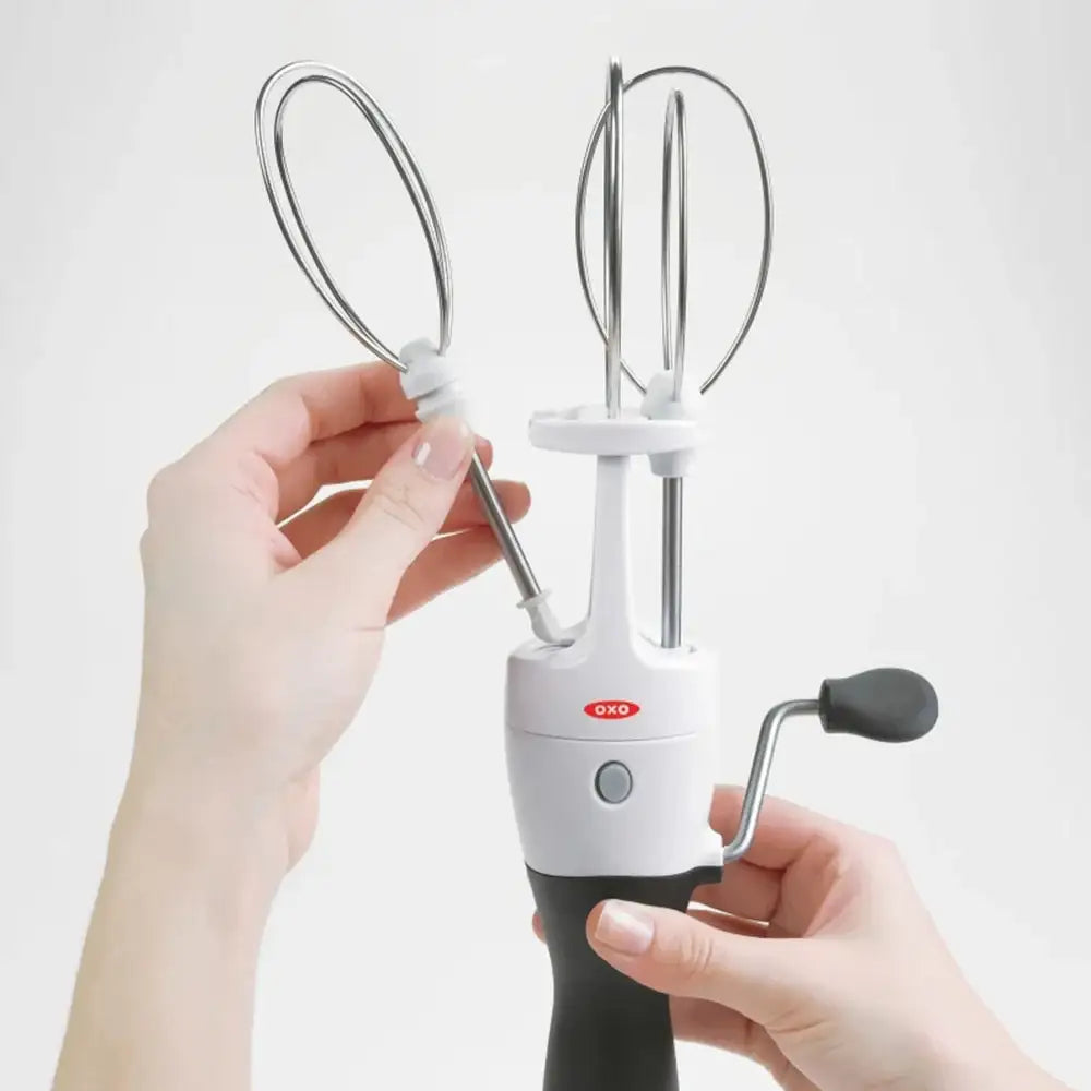 Handheld electric mixer with attachments held by a person against a white background