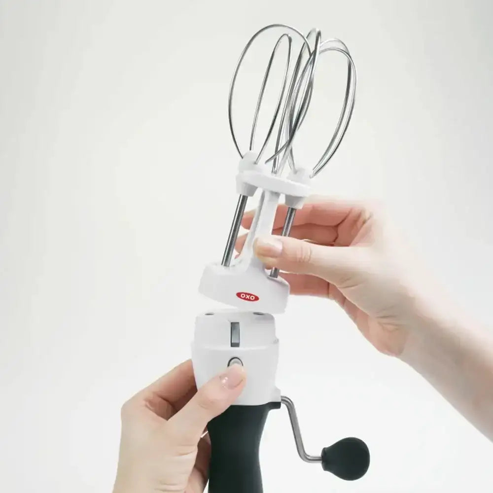Handheld mixer with whisk attachment held by a person on a white background