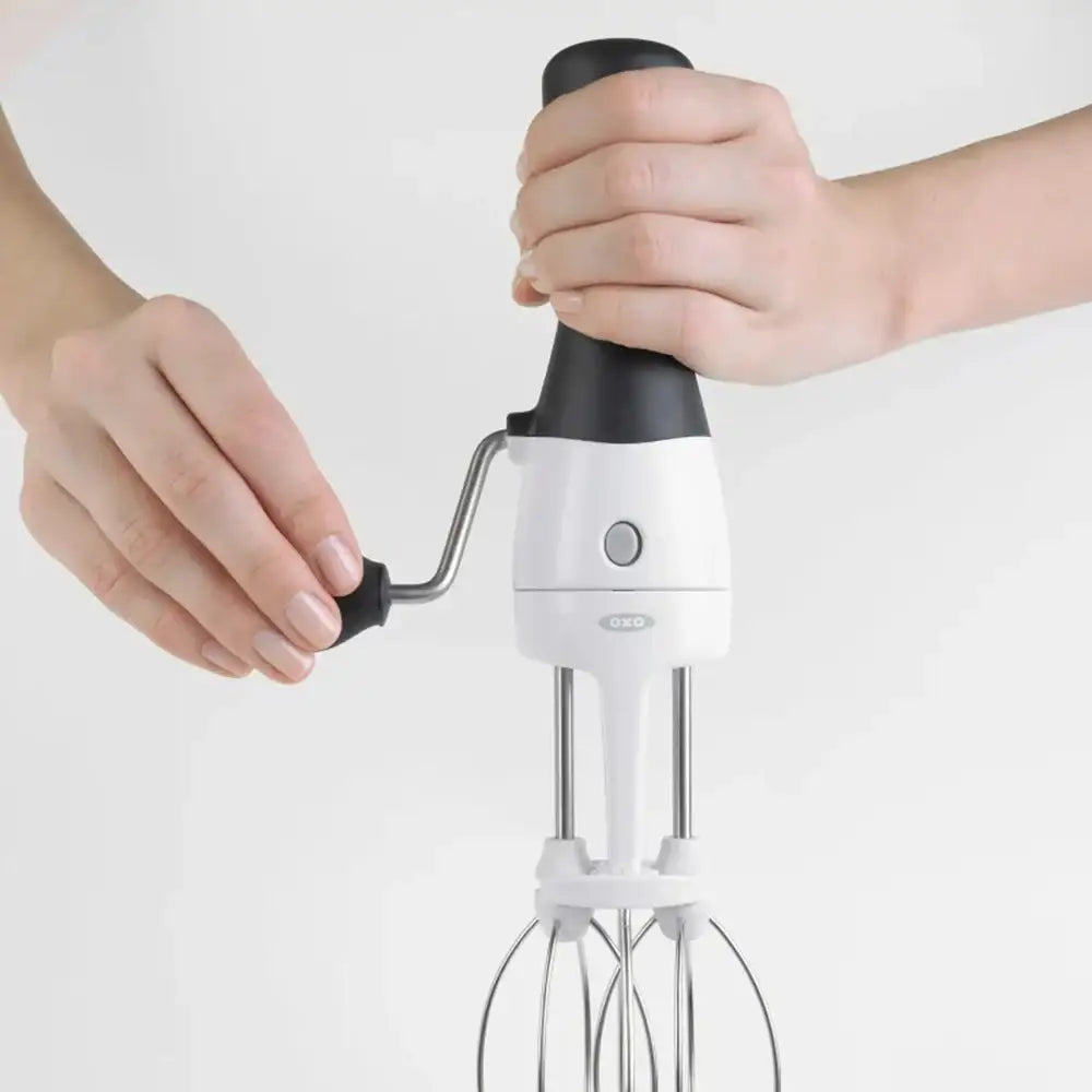 Handheld white mixer with black handle held by a person on a light gray background