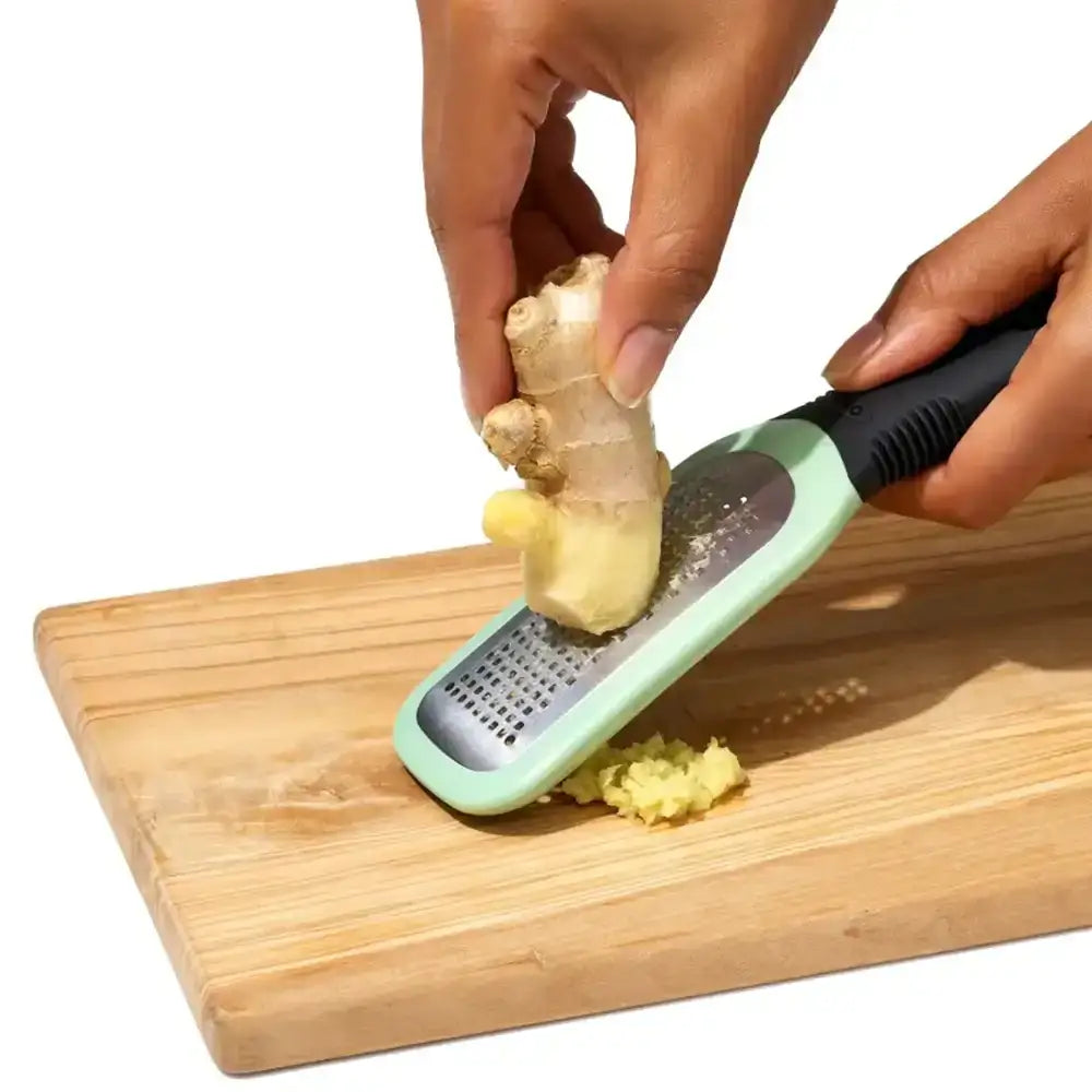 Person using a ginger grater on a piece of ginger over a wooden cutting board.