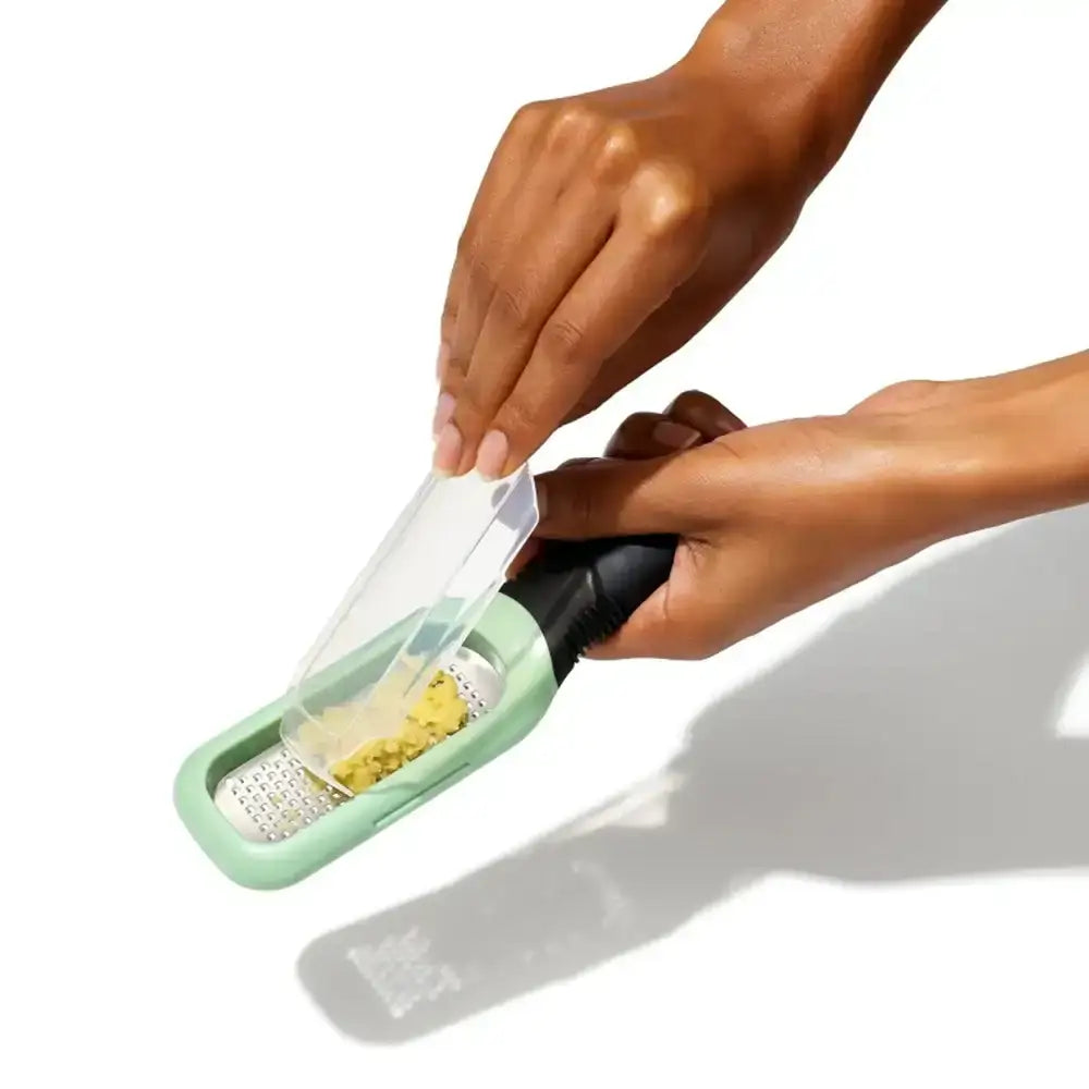 Hand using a green and black kitchen grater on a white background