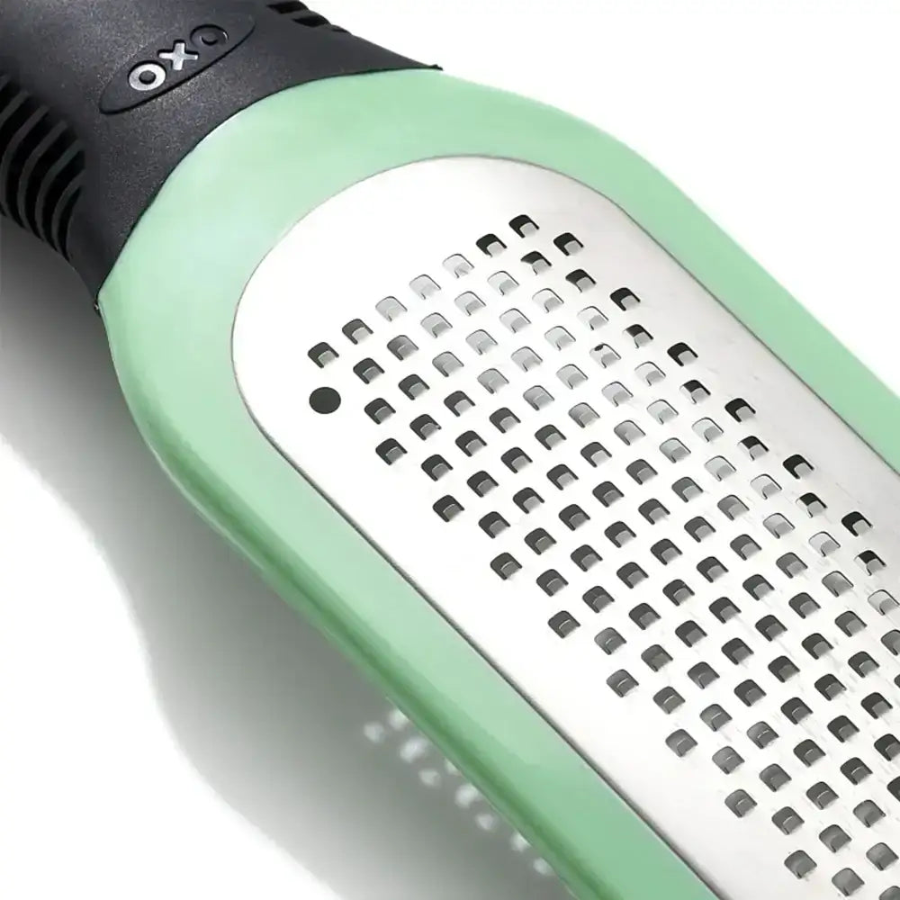 Close-up of a green and black OXO grater on a white background