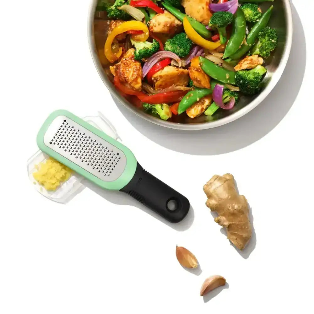 Grater next to a bowl of stir-fry with vegetables and chicken, on a white background