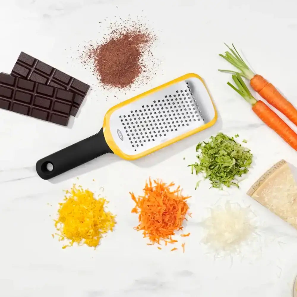 Grater with grated vegetables and chocolate on a white surface