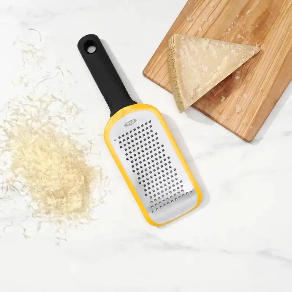 Yellow and black handheld grater with shredded cheese on a white surface